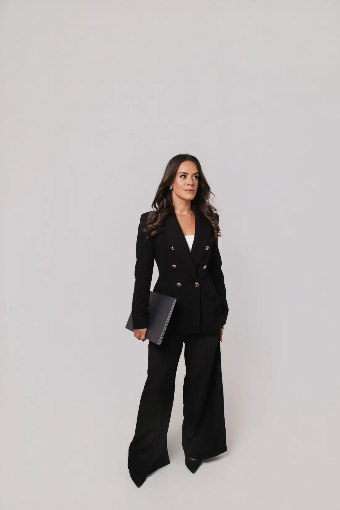 Dra. Camila Braga em traje profissional preto, segurando um notebook